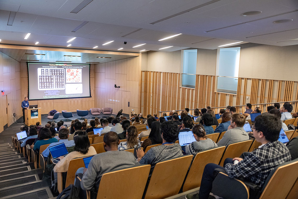 a full audience listening to a speaker with a visual presentation scree