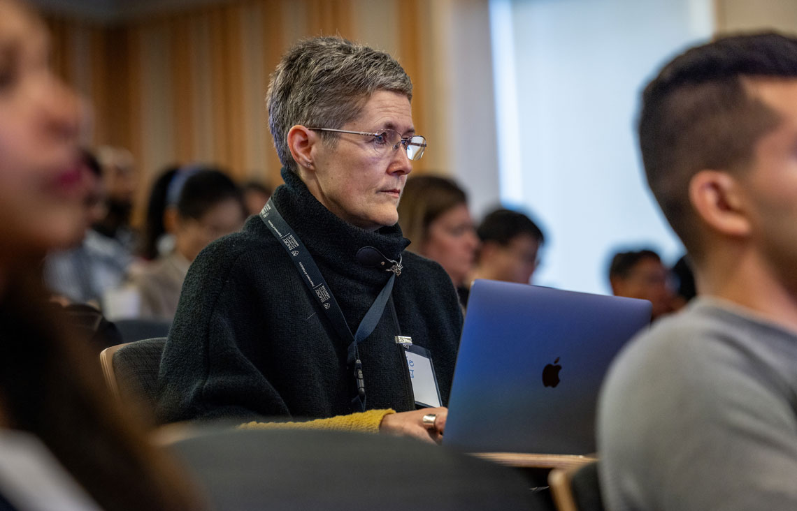 a seated woman listening while taking notes on a laptop